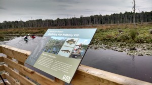 Boardwalk with signage and paddlers in the background